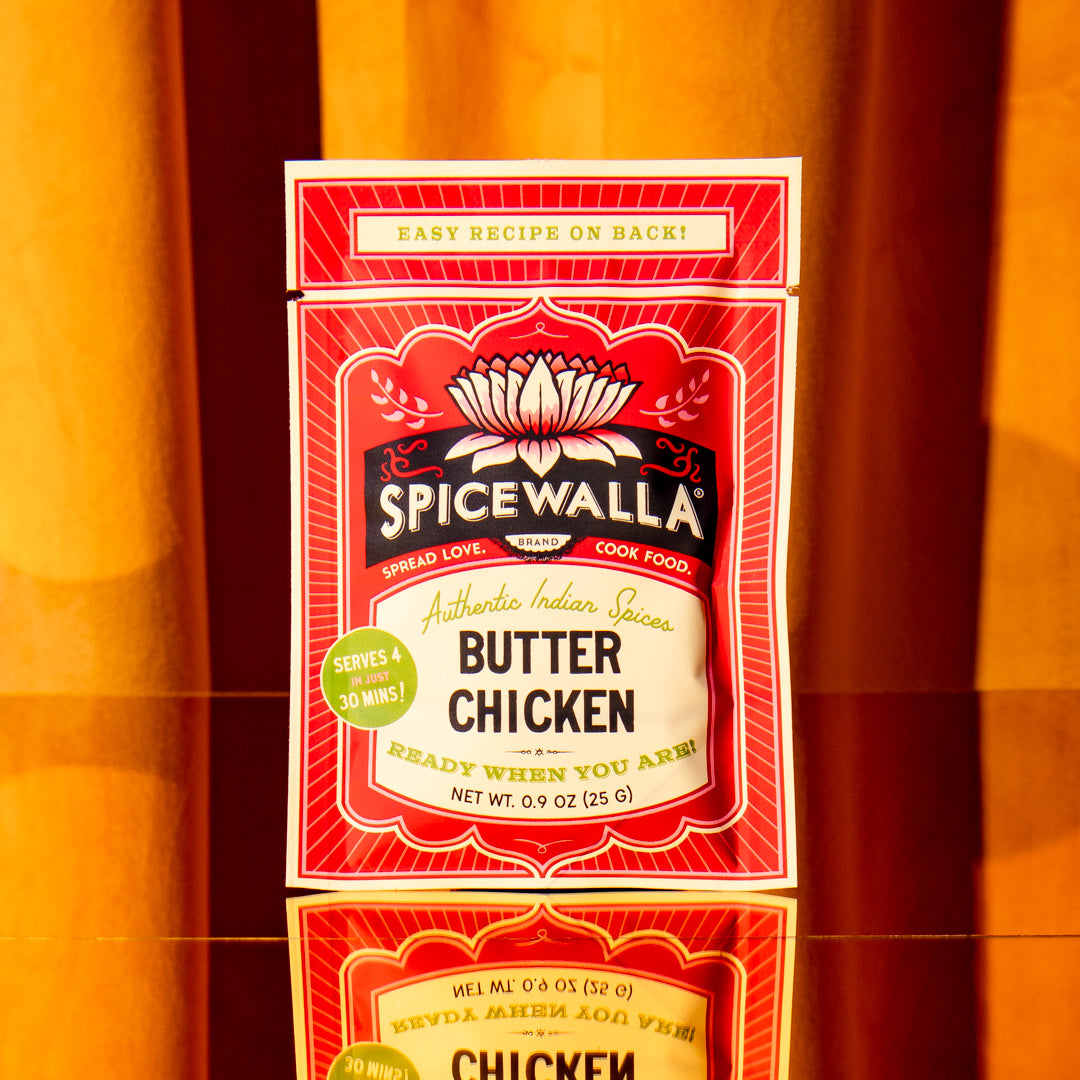A package of Spicewalla Butter Chicken Authentic Indian Spicy Sauce, featuring a red and cream design with a black Spicewalla logo, set against a warm orange background.