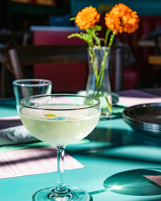 An olive oil martini on a teal tablecloth with marigolds in a small bud vase in the background (a tabletop at Chai Pani restaurant) 