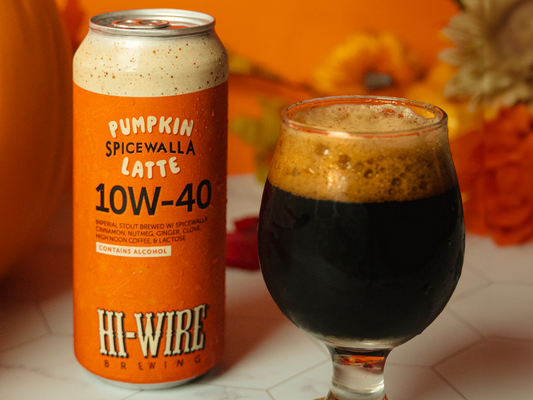 Can of Hi-Wire Pumpkin Spicewalla Latte 10W-40 beer with it poured in a glass and seasonal fall decor behind it.
