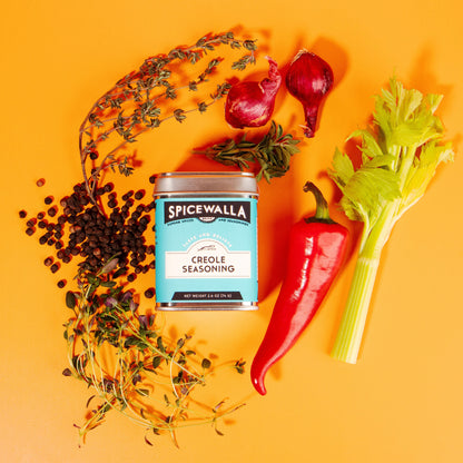 Spicewalla Goulash seasoning can surrounded by herbs, peppers, and vegetables on a yellow background