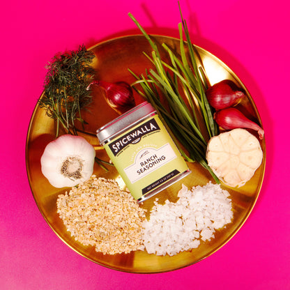 Spicewalla seasoning can on a gold plate with rice, vegetables, and herbs against a pink background