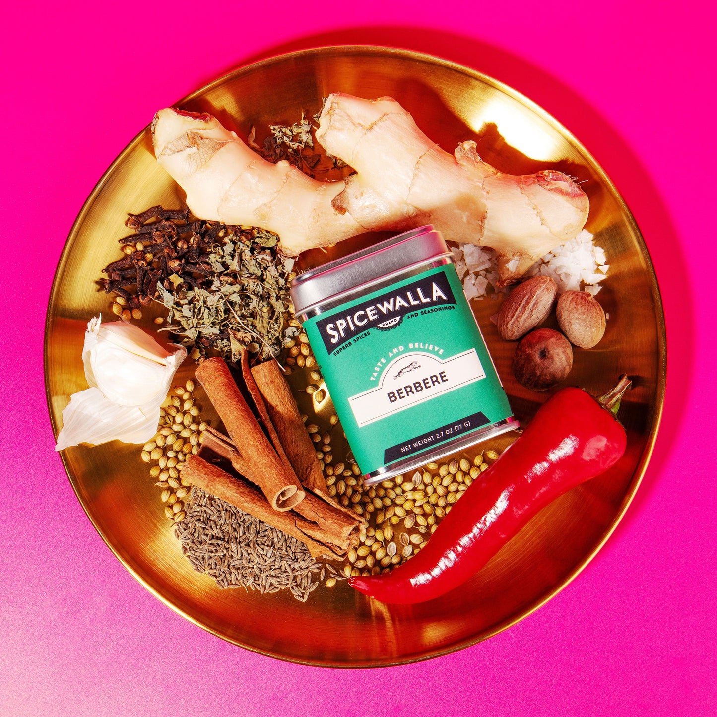 Spices and a box of 'Spicewalla' on a gold plate with a pink background