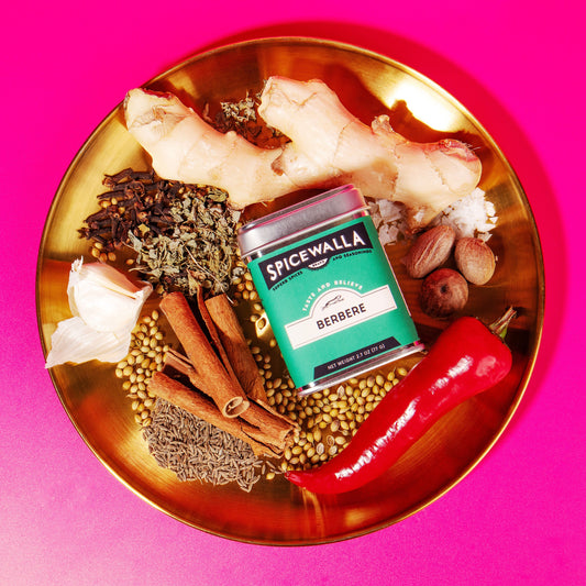 Spices and a box of 'Spicewalla' on a gold plate with a pink background