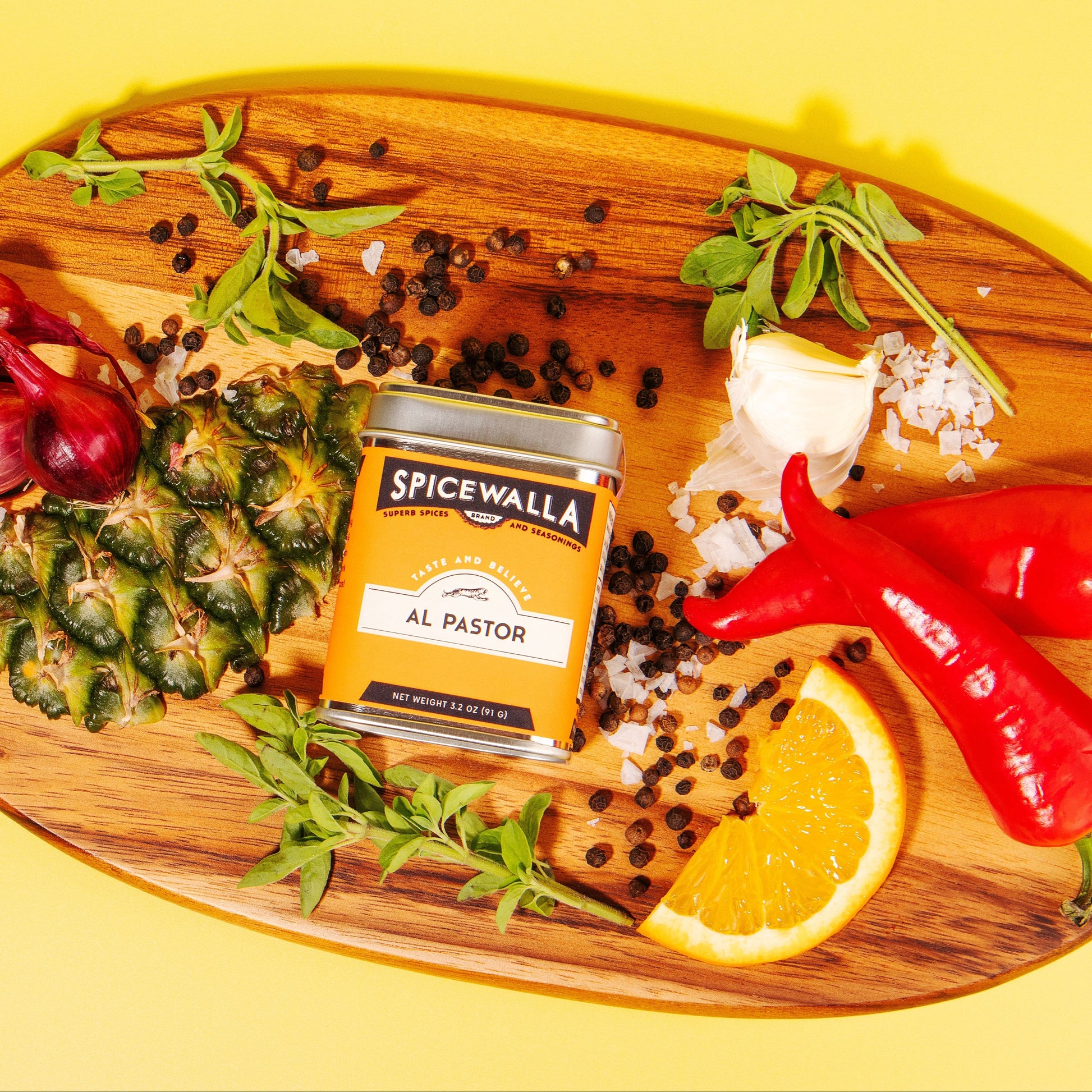 Spicewalla Al Pastor spice jar on a wooden cutting board with ingredients on a yellow background