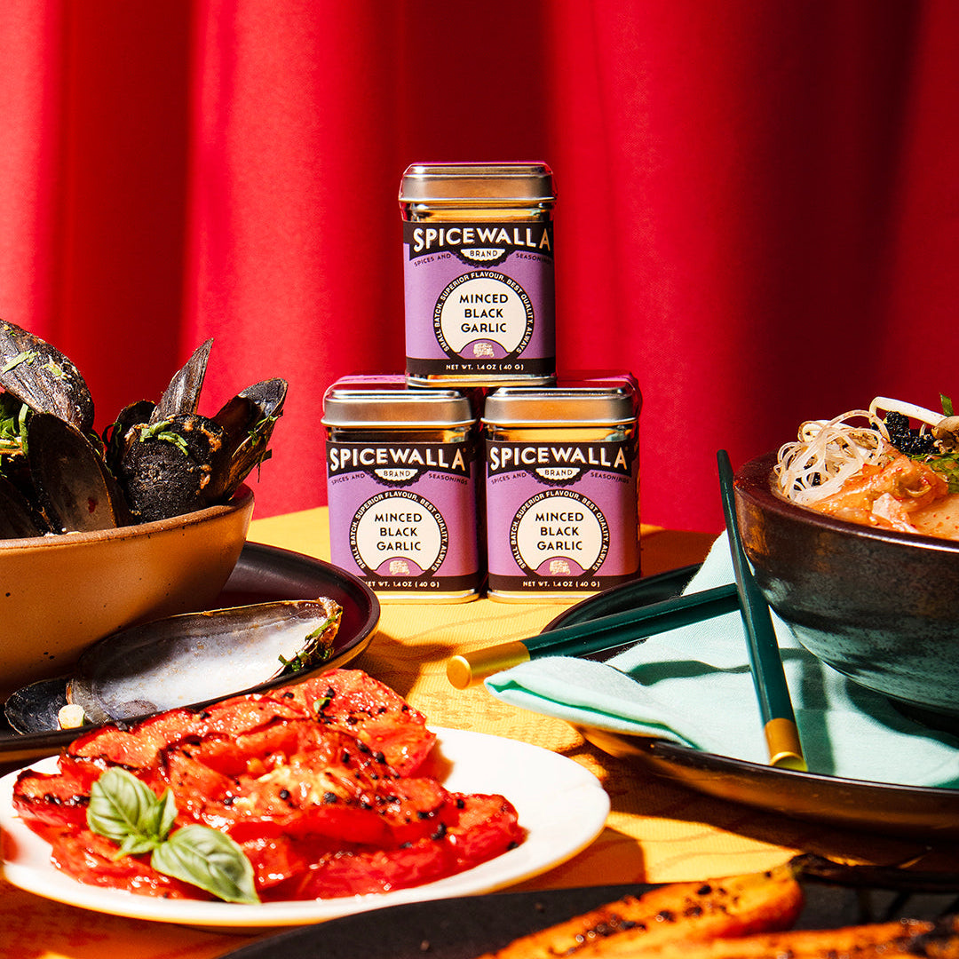 Spicewalla jars on a table with food items against a red curtain background