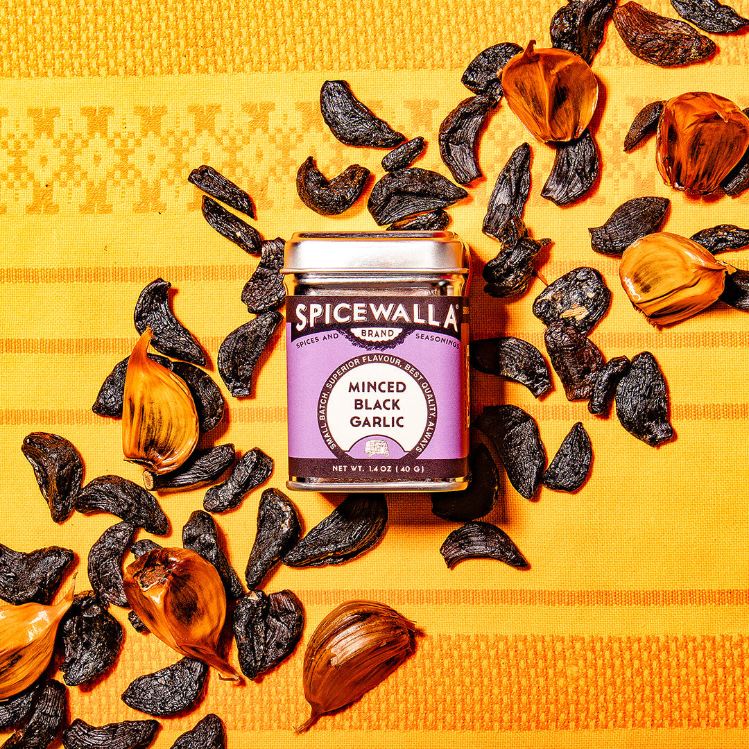 Spicewalla minced black garlic jar surrounded by garlic cloves on a yellow patterned background