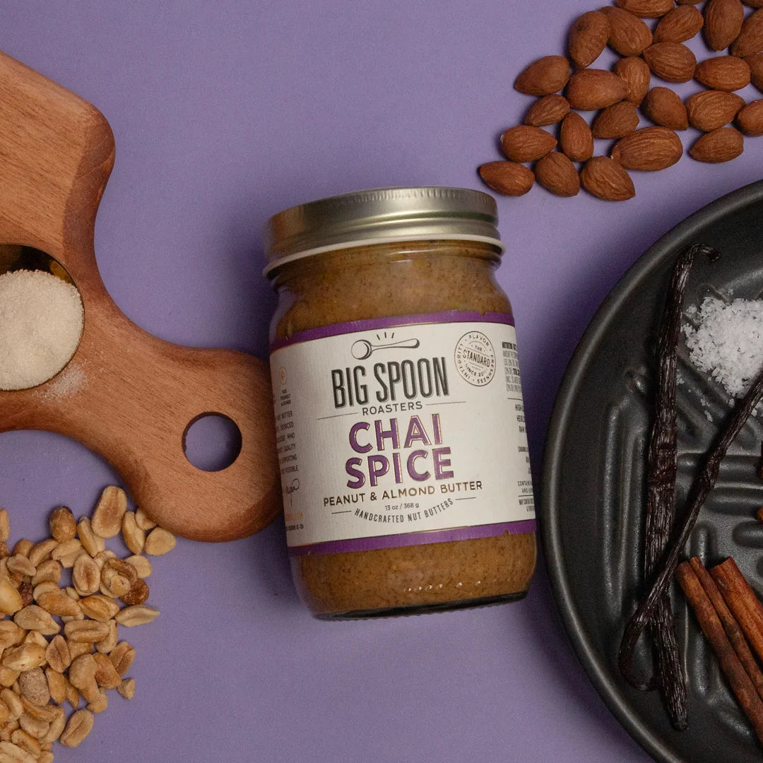 Jar of 'Big Spoon' Chai Spice peanut and almond butter on a purple background with ingredients around it.