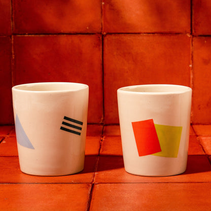 Three ceramic cups with geometric designs on a red tiled floor