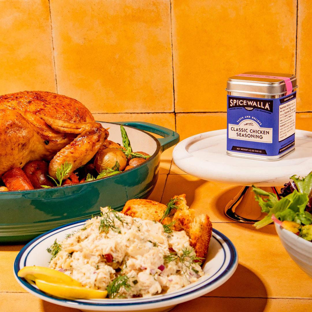 Roasted chicken with sides on a tiled countertop, featuring a container of SpiceWalla seasoning.