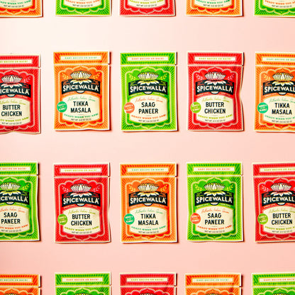 A grid of Spicewalla brand seasoning packets arranged in four rows on a pale pink background. The packets include Butter Chicken, Tikka Masala, and Saag Paneer flavors in red, orange, and green packaging.