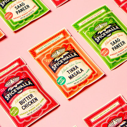 Multiple Spicewall seasoning packet packages arranged on a pink background, including Saag Paneer, Tikka Masala, and Butter Chicken flavors.