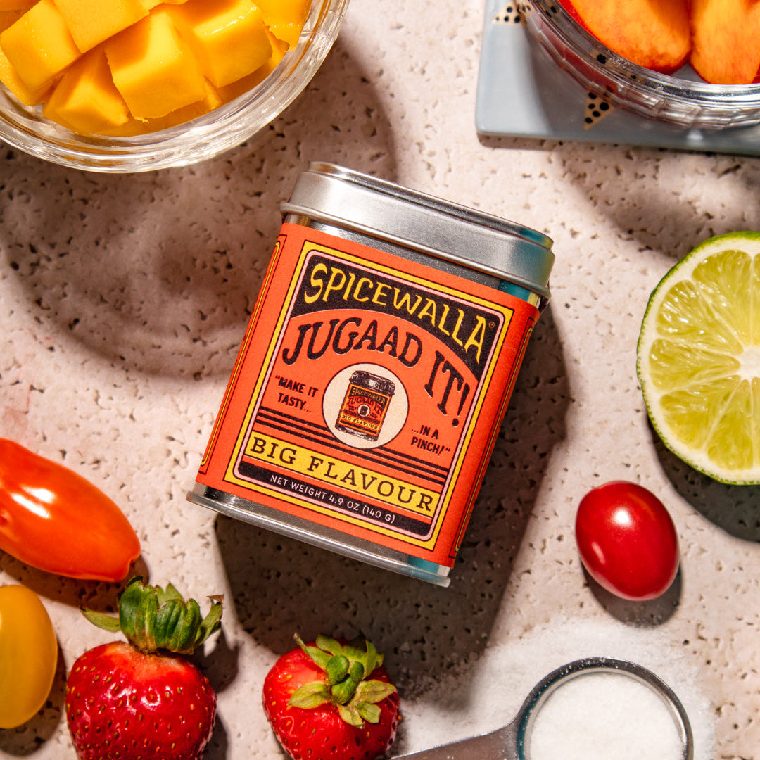 Spicewalla Jugaad It! can surrounded by fruit and ingredients on a textured surface