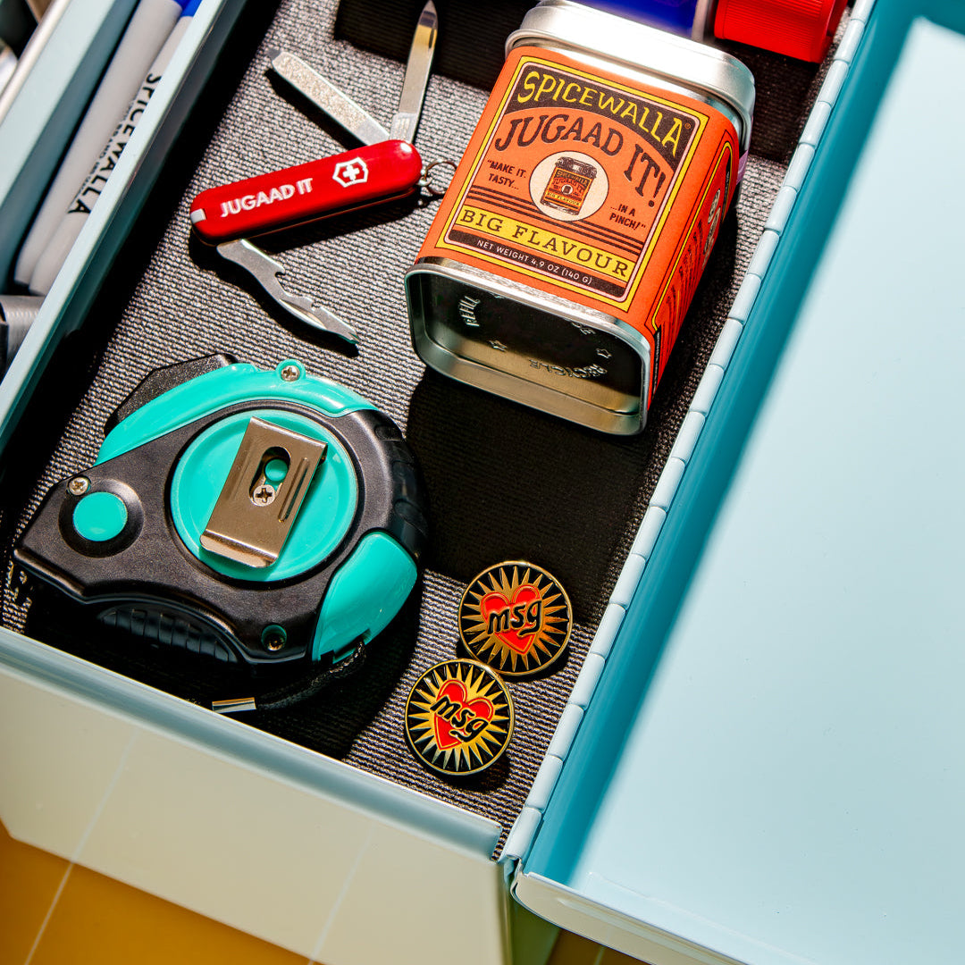 Open drawer with stationery items including a Swiss Army knife, tape measure, and Spice World Juggaad It can.