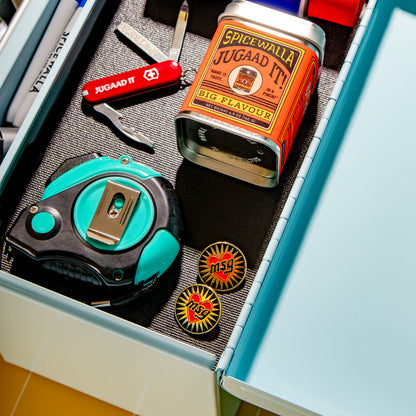 Open drawer with stationery items including a Swiss Army knife, tape measure, and Spice World Juggaad It can.