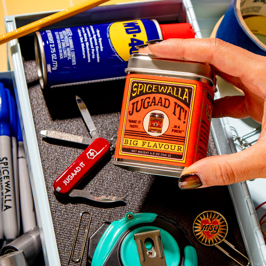 Spicewala Jugaad It! can held by a hand over a drawer with stationery items.