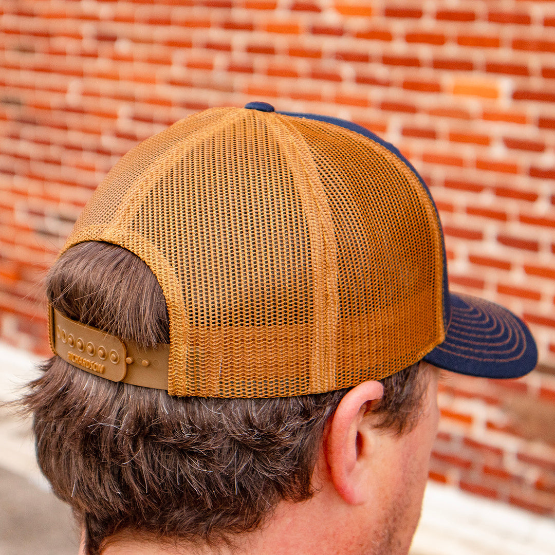 Person wearing a brown and blue cap against a brick wall