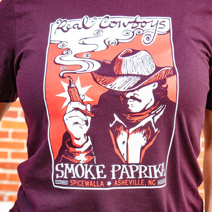 Maroon t-shirt with a graphic design of a cowboy smoking a cigarette, text 'Real Cowboys Smoke Paprika' on a brick wall background.