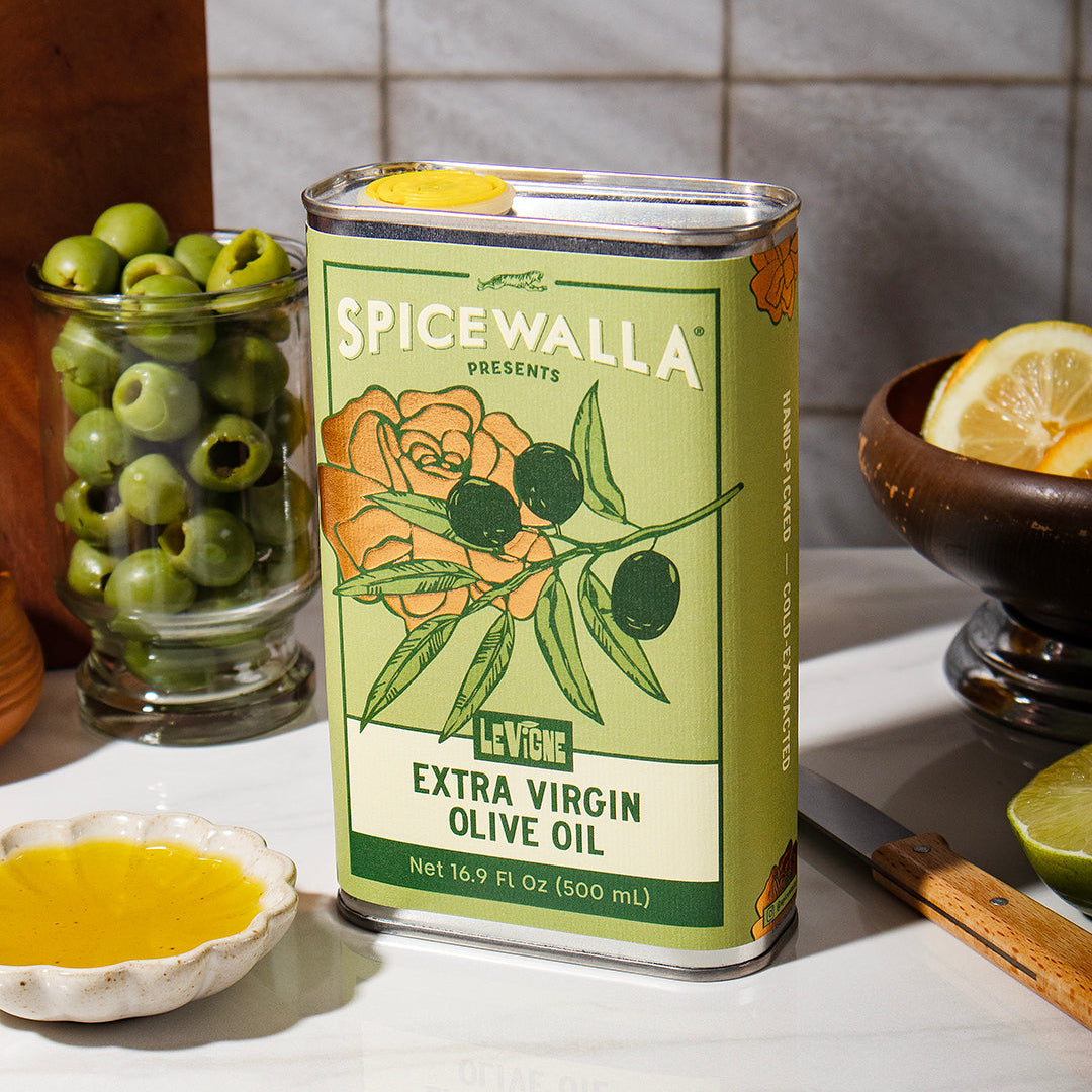 Spicewalla extra virgin olive oil can on a kitchen counter with olives and lemon slices.