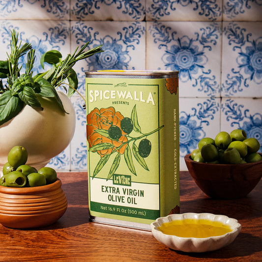 Spicewalla olive oil can with green olives and herbs on a wooden surface with tiled wall background