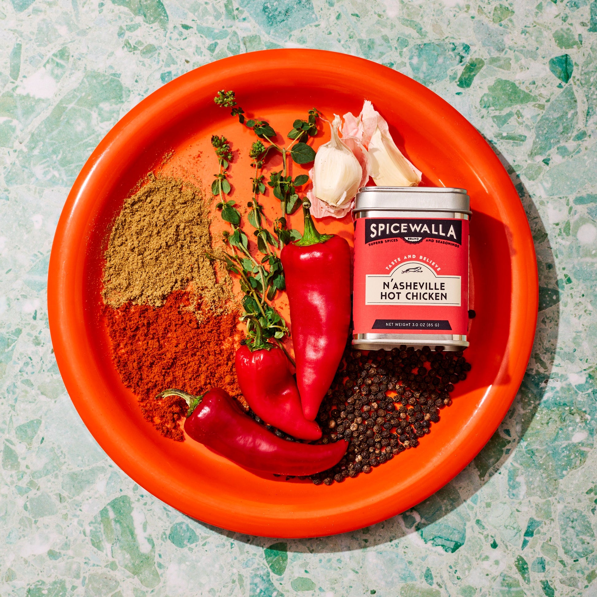 Spice container labeled 'Spicewalla' with red peppers, herbs, and spices on an orange plate.