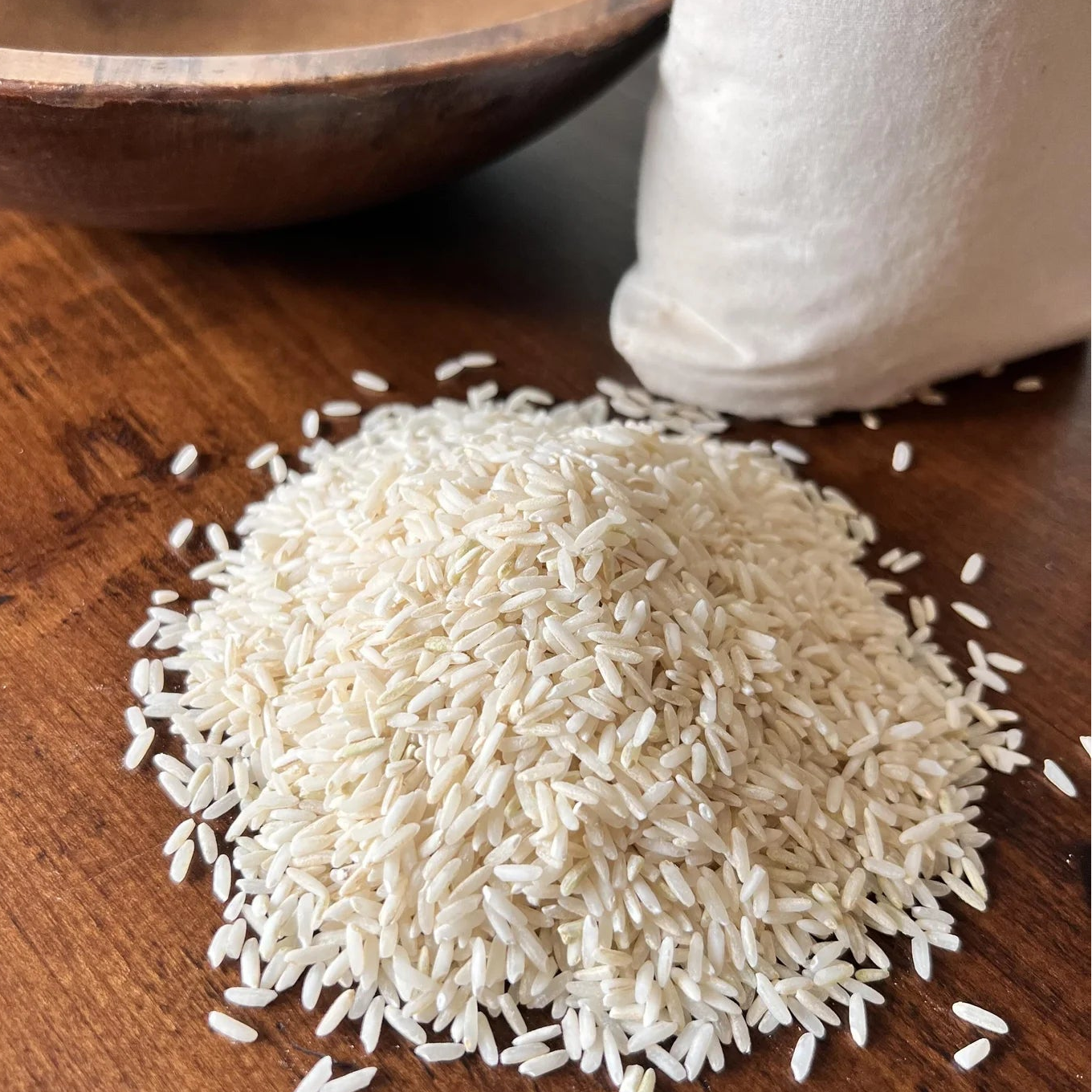 Carolina Gold White rice on a wooden surface with a wooden bowl and white container in the background.