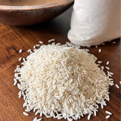 Carolina Gold White rice on a wooden surface with a wooden bowl and white container in the background.