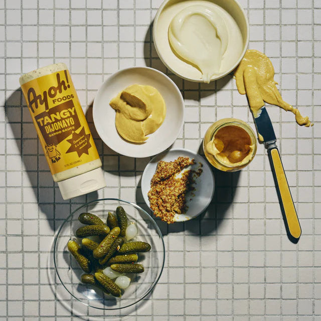 Tangy Djonay sauce with a knife, pickles, and bread on a tiled surface
