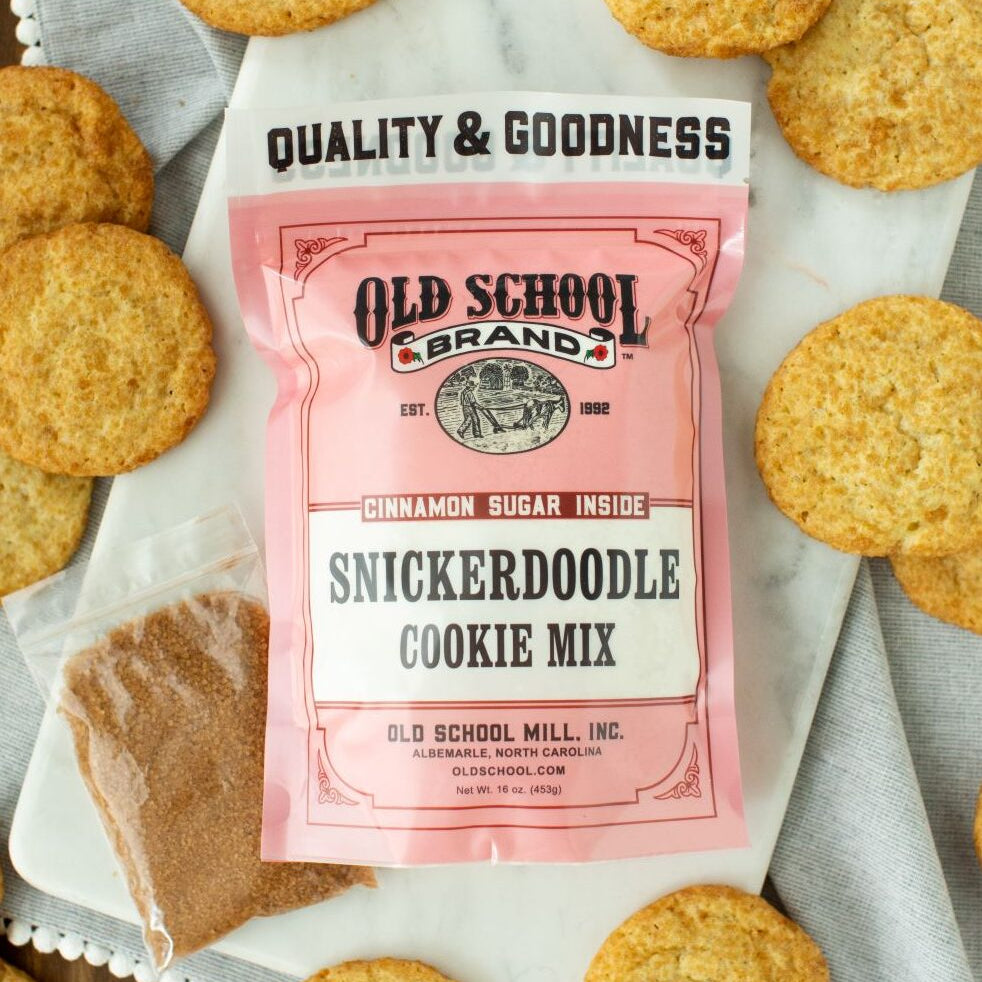 Pink packet of Old School Brand Snickerdoodle Cookie Mix surrounded by cookies on a marble surface