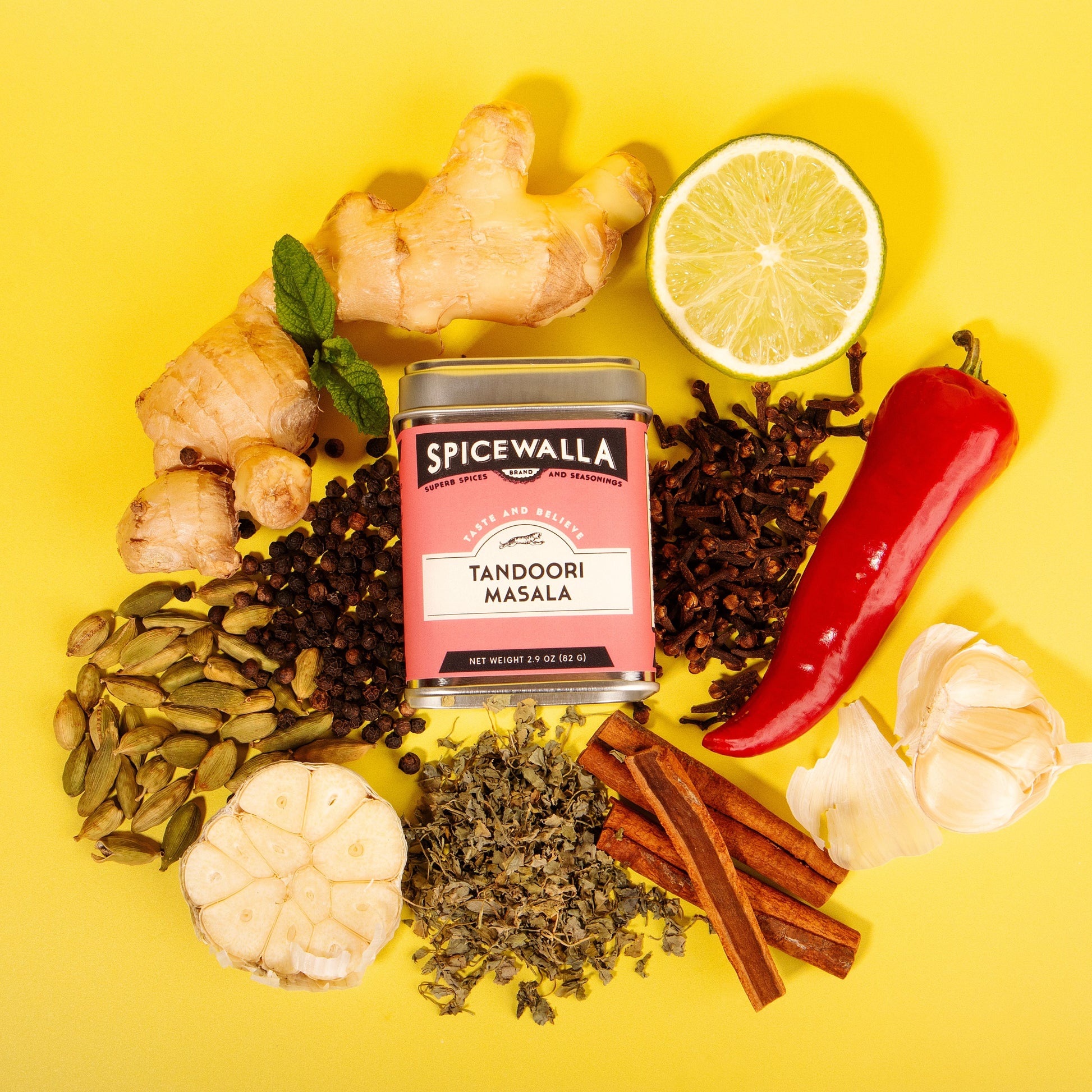 Spicewalla Tandoori Masala can surrounded by spices and herbs on a yellow background